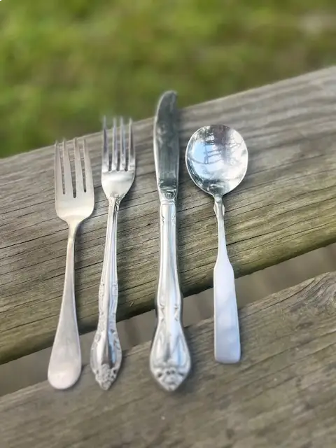 dessert fork, dinner fork, knife and spoon displated on a wood bench