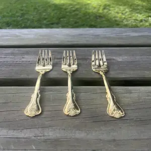 3 dinner forks gols finish sitting on a bench.