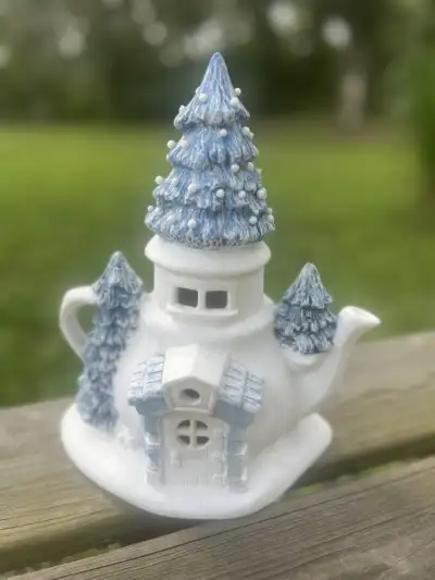 mismatch tea pots rentals | The Tea Party Company Cute white and blue christmas teapot with a tall tree with snow on the lid and two trees on the side and a door and a window.